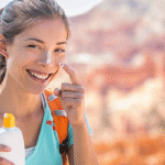 Smiling woman hiking outdoors and applying sunscreen to her face.